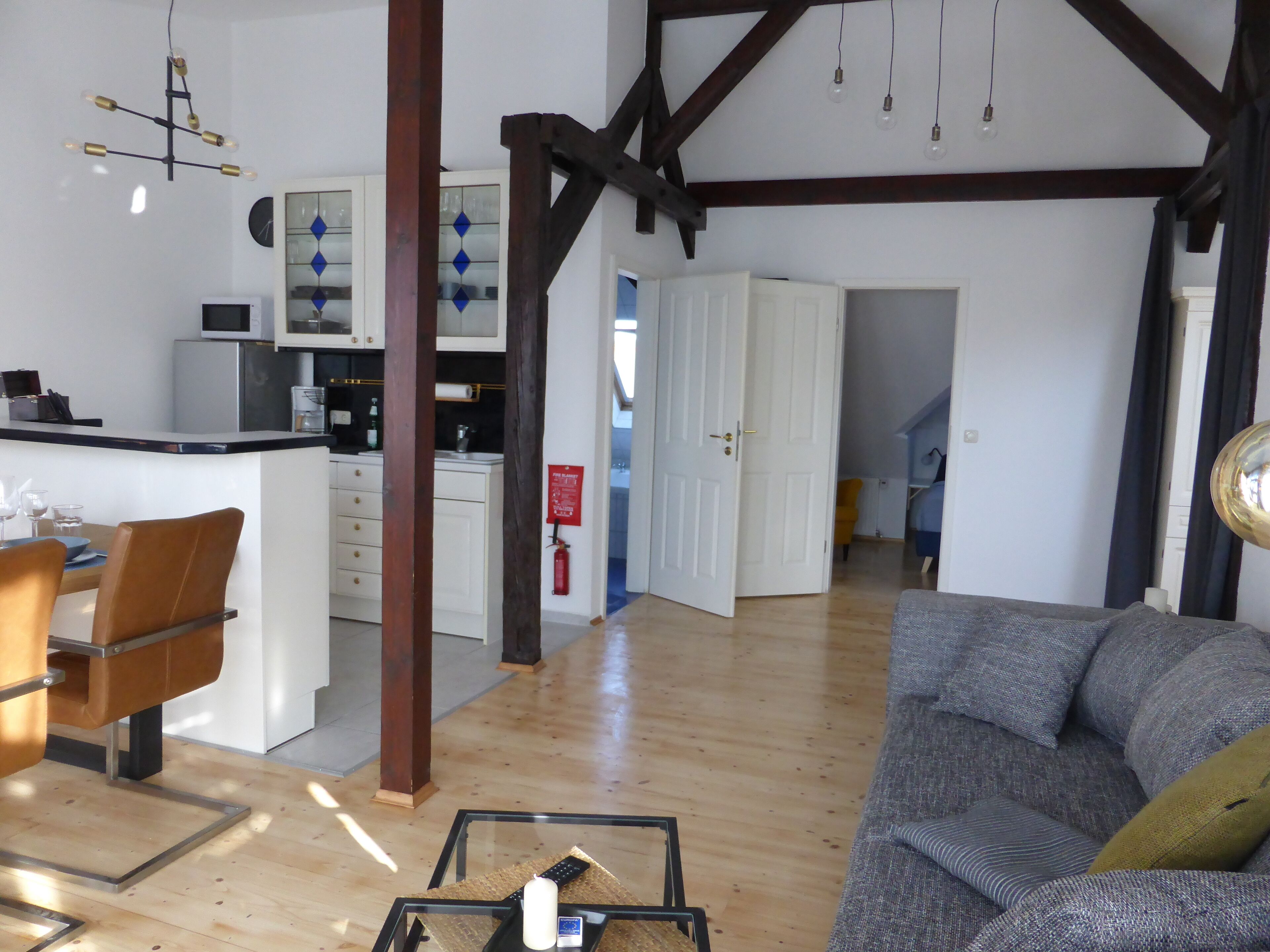 Amplia sala de estar con sofá, mesa de comedor con sillas, zona de cocina con microondas y escalera que lleva a otra habitación.