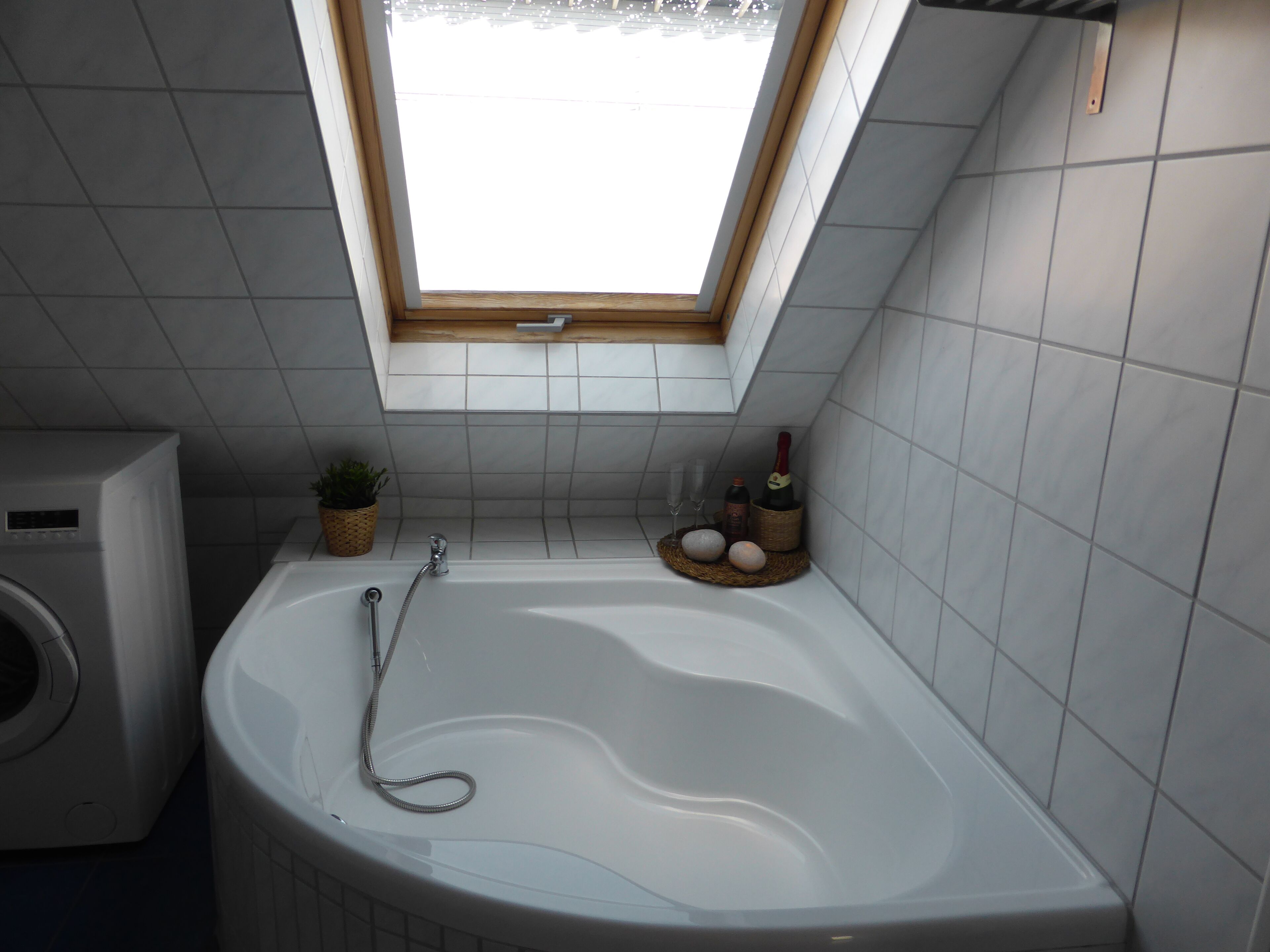 Ein Badezimmer mit integriertem Fenster, einer Badewanne, einer Waschmaschine und einem kleinen Topfpflanzen.