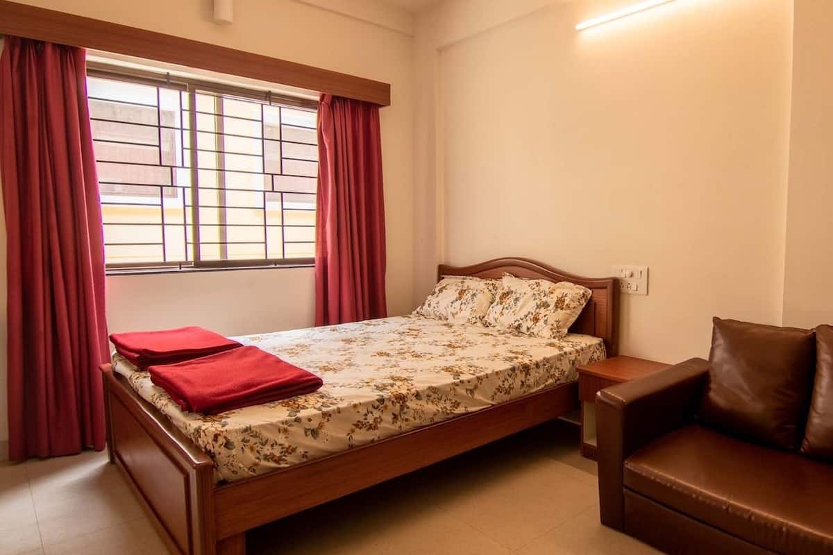 A bedroom with a bed, a nightstand, a brown leather sofa, and a window with curtains.