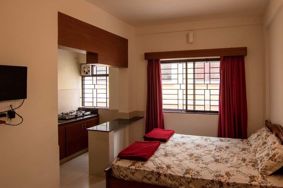 A compact room with a bed, a small desk, a television, and a window with curtains.