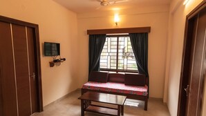 Una habitación con una cama, una mesita, un televisor montado en la pared y una ventana con cortinas.