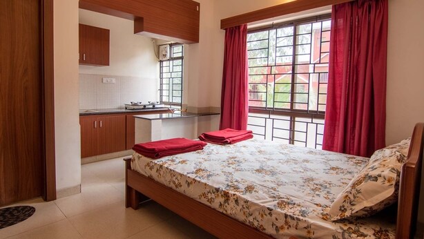 Un dormitorio con cama, una kitchenette pequeña y un ventanal con cortinas.