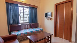 Una habitación con un banco de madera, una mesa pequeña, un televisor montado en la pared y una puerta de madera.
