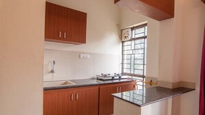 Una cocina con armarios de madera, estufa a gas, ventana con rejas y una cortina roja.