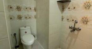 A bathroom with a toilet, a shower, and tiled walls with a floral pattern.