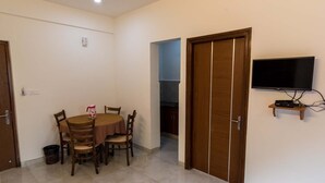 Un comedor con una mesa redonda y sillas, un televisor sobre un mueble bajo, y una puerta que da a otra habitación.