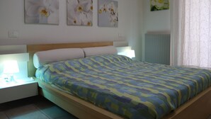 Ein Schlafzimmer mit einem hölzernen Kopfteil, einer gemusterten Bettdecke und drei an der Wand befestigten Blumenbildern.