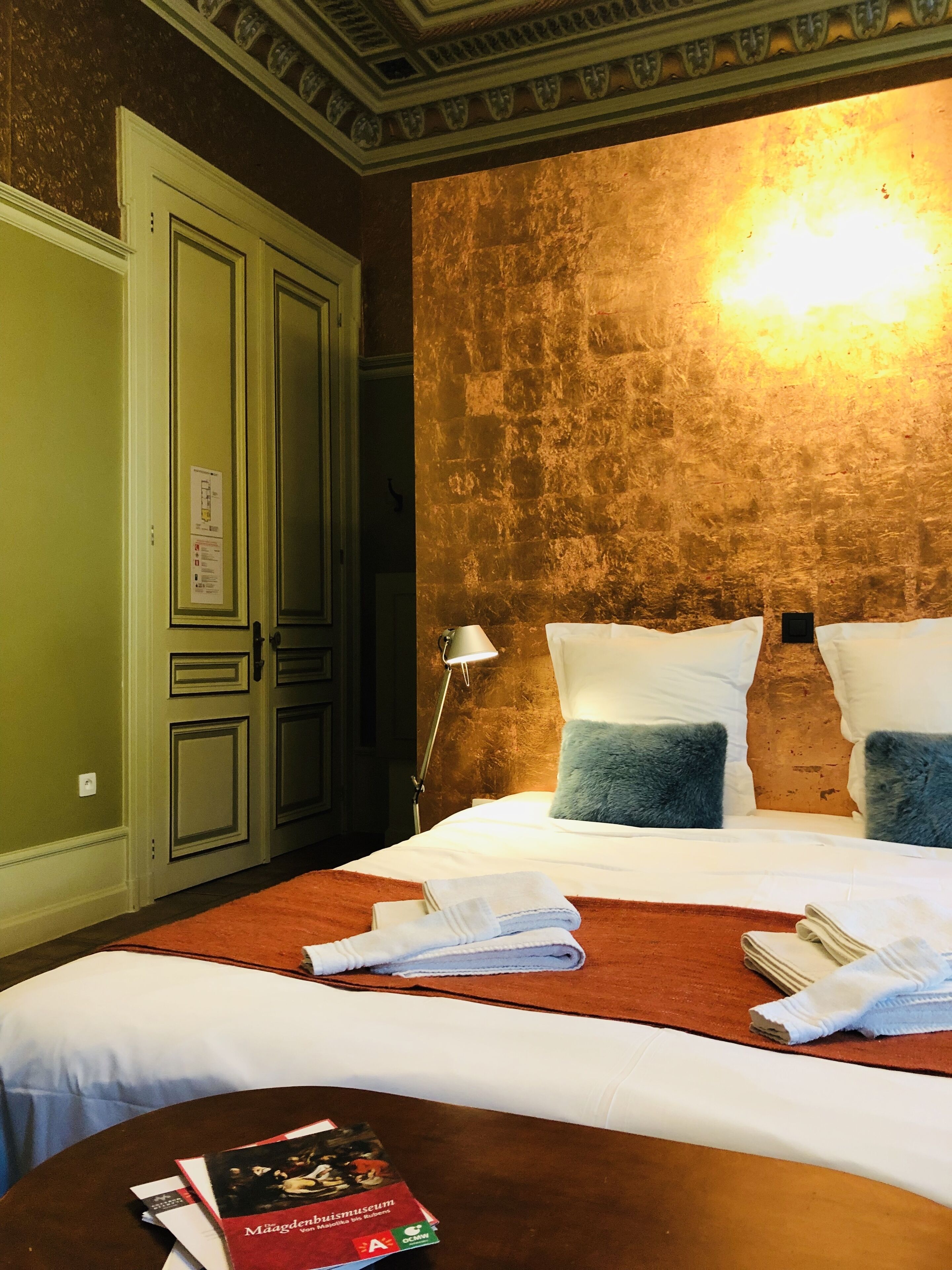 Habitación de hotel con una cama grande, una mesita de noche, una lámpara y una pared con textura.