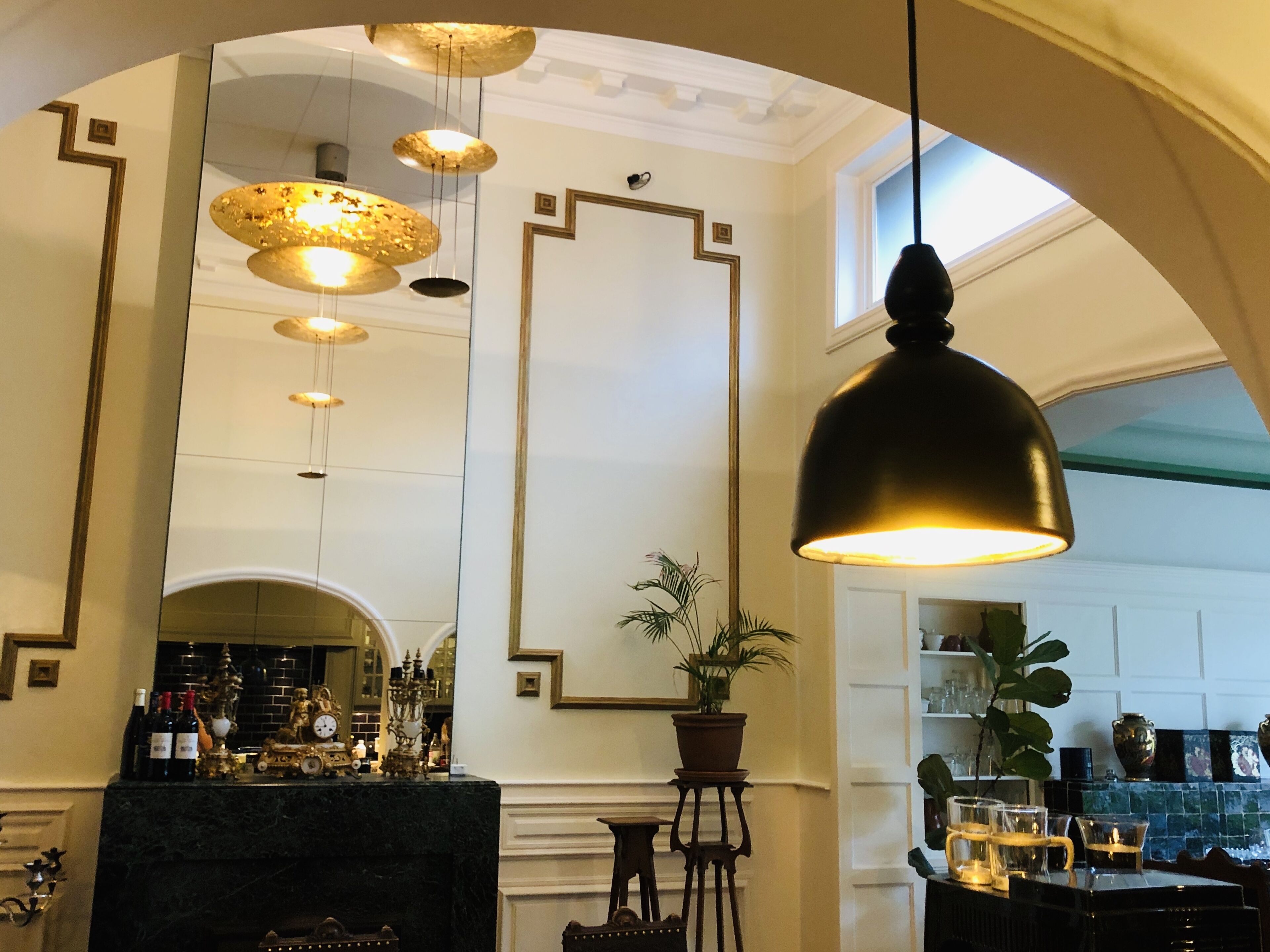 Een bar met een marmeren toonbank, hangende lampen en een potplant.