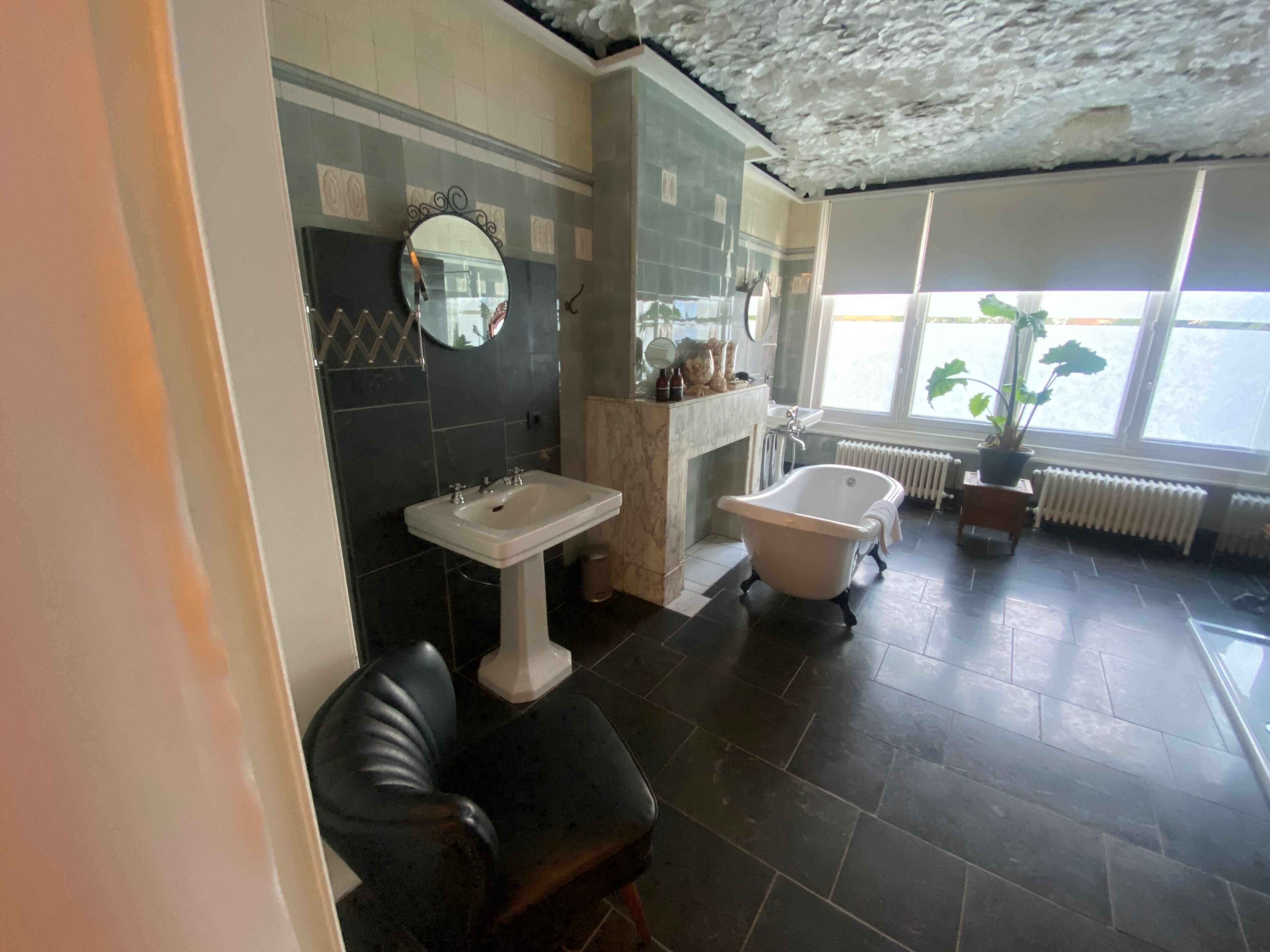 A bathroom with a bathtub, a sink, a mirror, and a potted plant by the window.