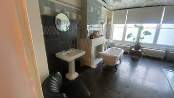 A bathroom with a bathtub, a sink, a mirror, and a potted plant by the window.