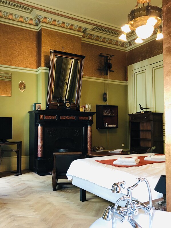 A hotel room with a large bed, a fireplace, a mirror, a television, and a chandelier. - B&B Au Lit Jerome (Antwerp)