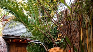 Deux vélos équipés de paniers en osier sont garés dans un jardin, avec un mur de pierre et une porte en bois en arrière-plan.