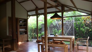 Un espace de salle à manger en bois, avec une table et des bancs, entouré d’un mur de pierre et d’une végétation luxuriante.