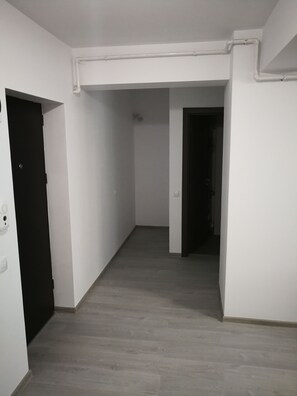 Ein Flur mit weißen Wänden, einer dunklen Tür links und einem Lichtschalter an der Wand.