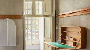 Ein Zimmer mit einem Holztisch, einem an der Wand befestigten Kleiderhaken und einem Fenster mit geöffneten Rollläden.