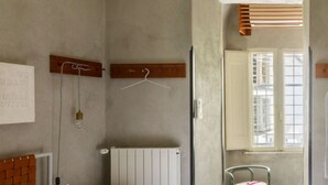 Ein Zimmer mit Heizkörper, einem Bett mit Holz-Kopfteil, einer Pendelleuchte, einem Fenster mit Jalousien und einem Sessel.