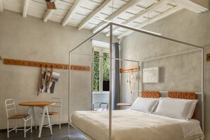 Een slaapkamer met een hemelbed, een kleine tafel met stoelen en een raam met uitzicht op groen.