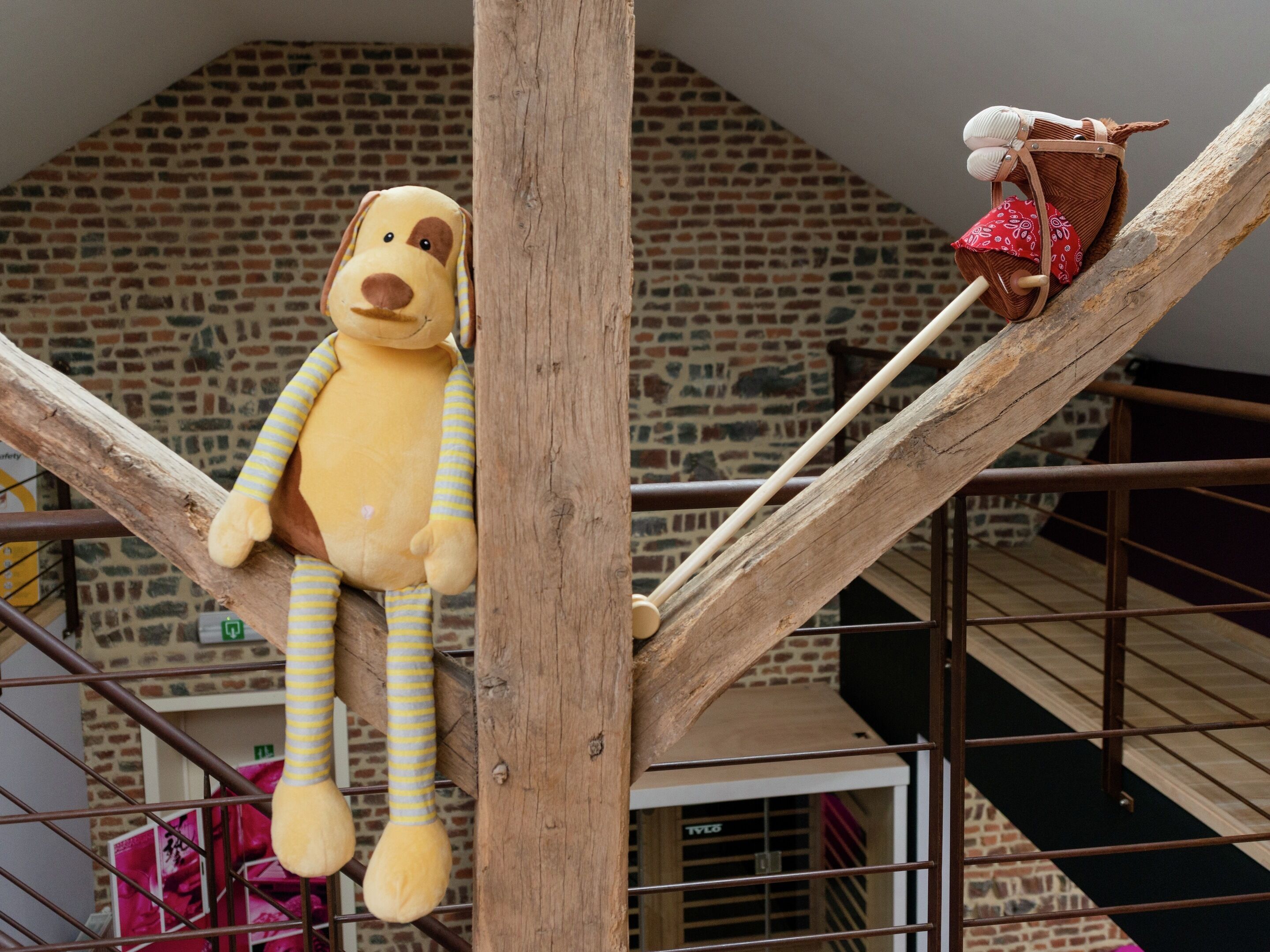 A stuffed dog toy on a wooden structure with a brick wall in the background.