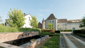 A courtyard with a brick retaining wall, a pathway, and a stone building with a tower. - Magnificent Character Cottage with Spa Tub near Marche-en-Famenne (Marche-en-Famenne)