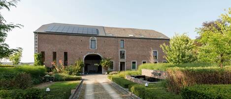 A large brick building with a central archway, solar panels on the roof, and a gravel pathway leading to the entrance.