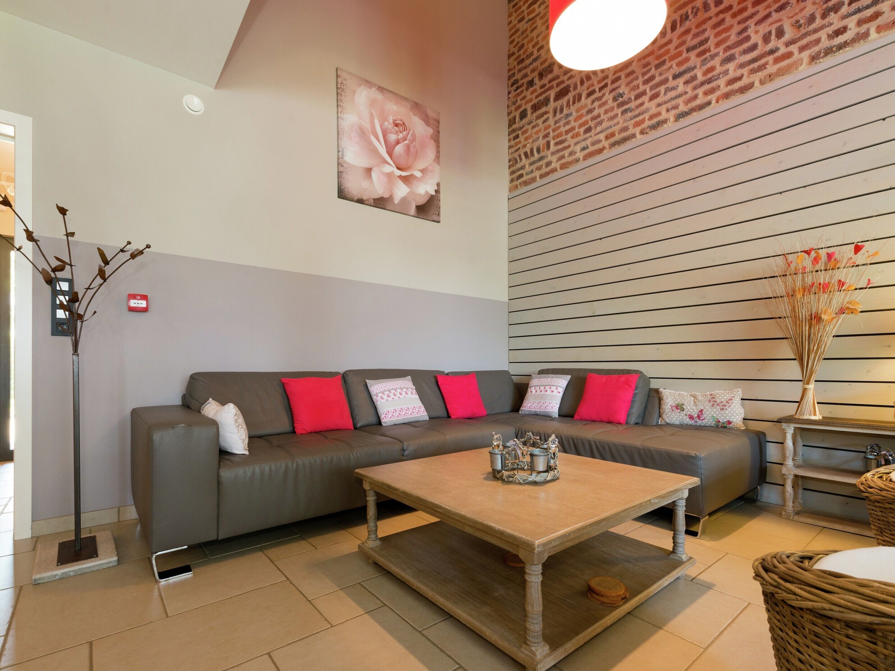 Uma sala de estar moderna com um sofá cinzento, almofadas vermelhas, uma mesa de centro de madeira e um quadro pendurado na parede com uma rosa.