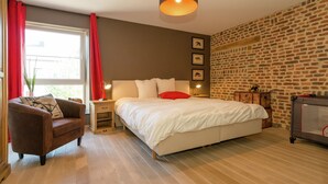 A bedroom with a large bed, a nightstand, a lamp, a chair, and a brick-patterned wall. - Magnificent Character Cottage with Spa Tub near Marche-en-Famenne (Marche-en-Famenne)