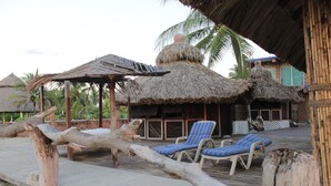 A beachside resort with thatched-roof huts, lounge chairs, and a wooden deck.