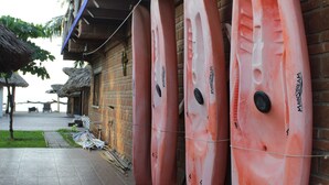 Kayaks lined up against a brick wall, a tiled walkway, and a building with a blue awning.