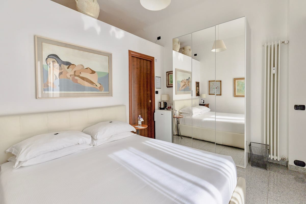 A bedroom with a bed, a wooden door, a mirror, and a white radiator.