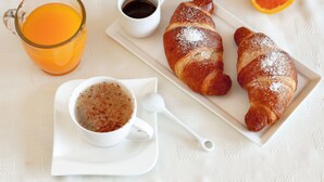 A breakfast setting with a croissant, a glass of orange juice, and a cup of coffee on a white tablecloth.