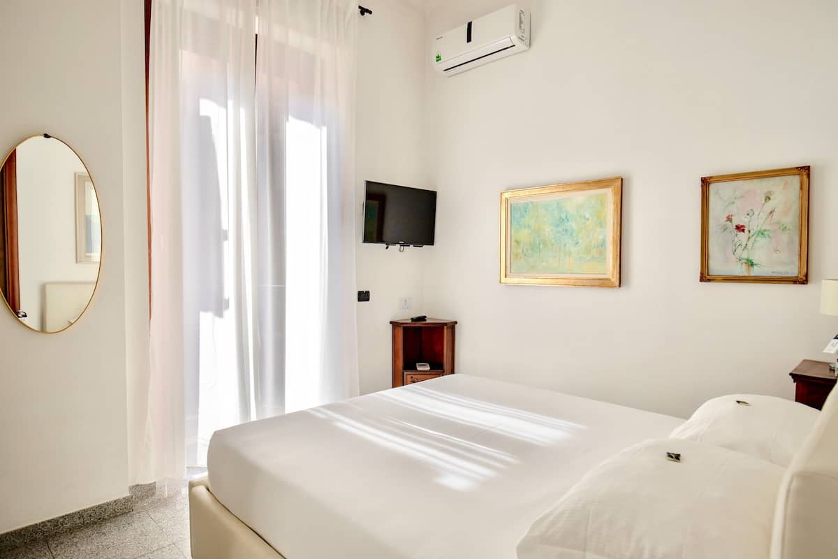 A hotel room with a bed, a television, a painting, and an air conditioning unit.