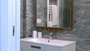 A bathroom with a marble wall, a white vanity with a sink, a mirror with an ornate frame, and a towel rack.