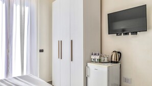 A hotel room with a bed, a wardrobe, a minibar, a television, and a window with curtains.