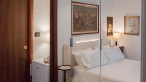 A hotel room with a bed, a small table, a lamp, a painting, and a door. - Aiello Suites Milan (Milan)