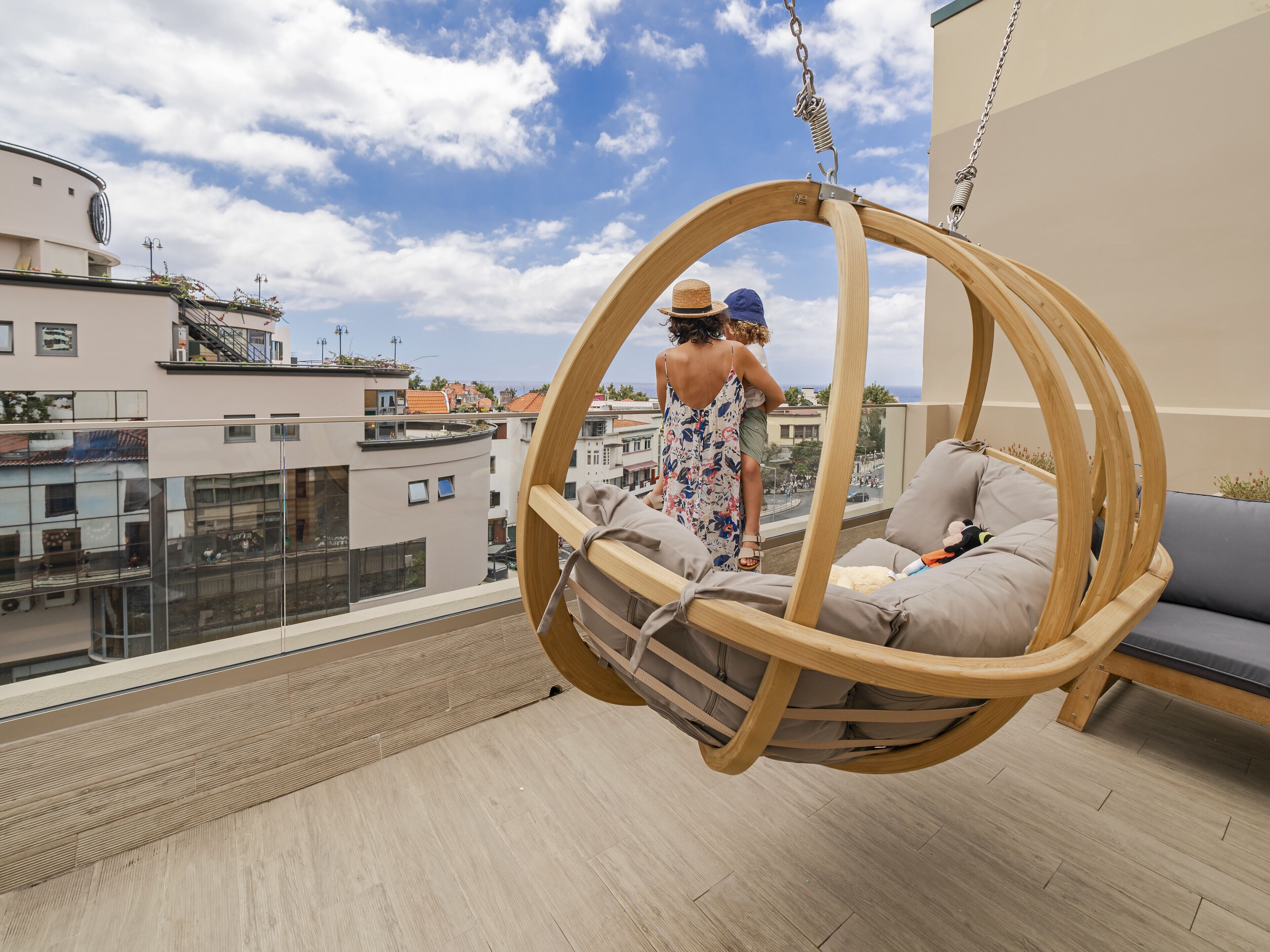 A wooden swing chair on a balcony with a city view.