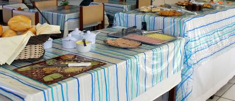 A buffet setup with various food items and serving utensils on tables covered with striped tablecloths.