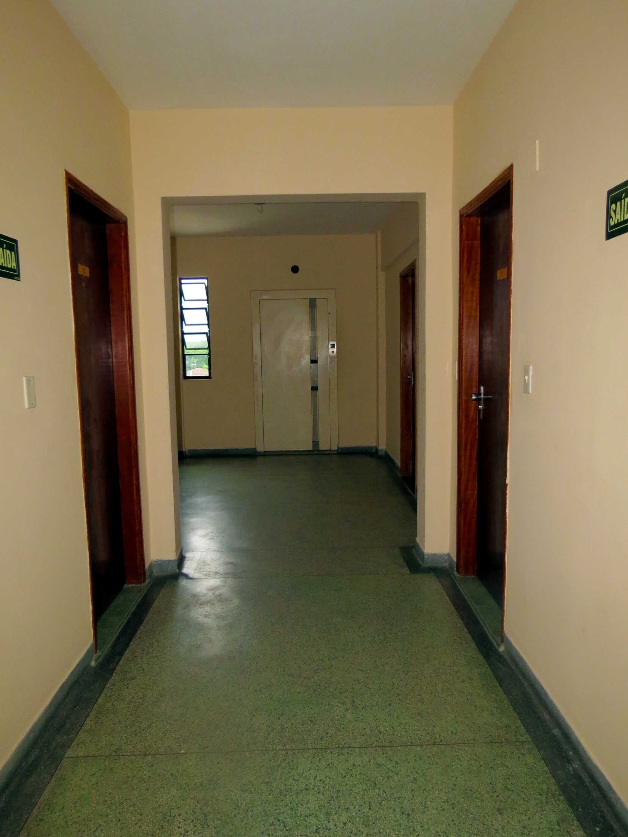 Um corredor com piso verde, portas de madeira e uma janela com persianas.
