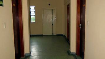 Um corredor com piso verde, portas de madeira e uma janela com persianas.