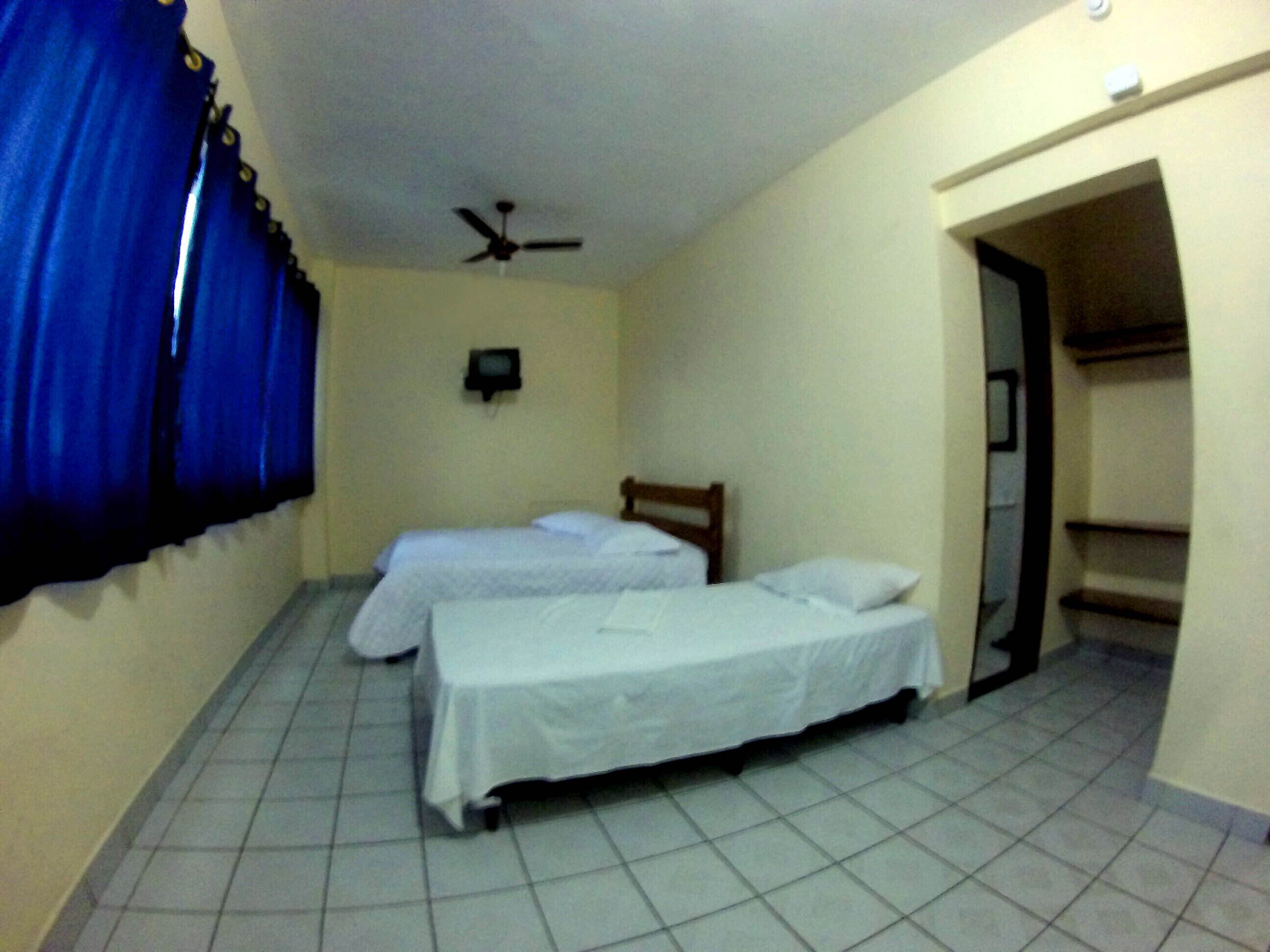 A room with two beds, a ceiling fan, and a small TV on the wall.