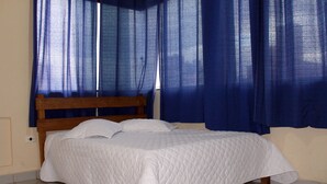 A bed with a wooden headboard, white bedding, and blue curtains. - Hotel Harmonia (Praia Grande)