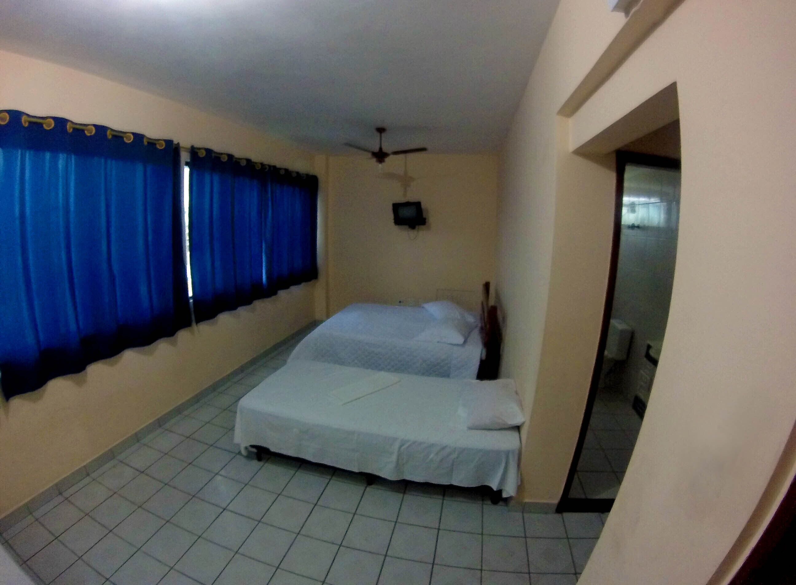 Quarto com duas camas, um ventilador de teto e uma TV na parede.