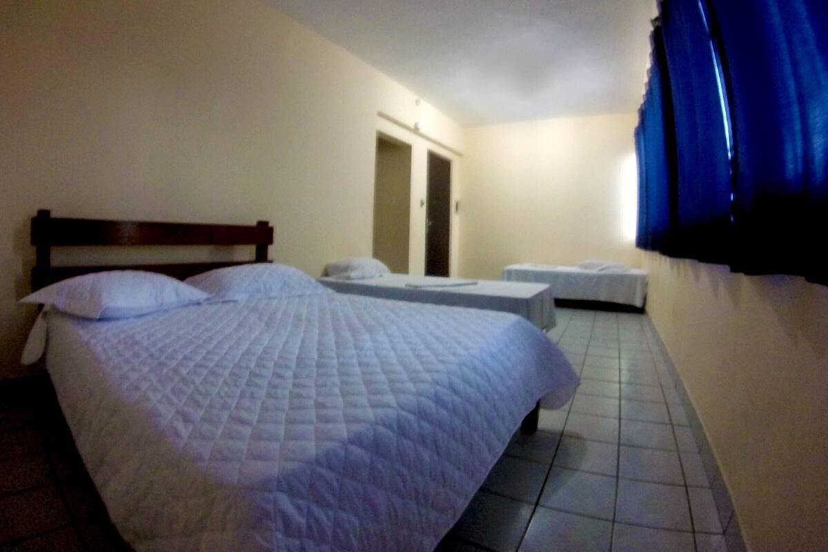 Une chambre d’hôtel avec un grand lit, un lit plus petit, une armoire et une fenêtre avec des rideaux.