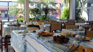 A buffet setup with various desserts and bread, tables covered with striped tablecloths, and chairs arranged around the tables. - Hotel Harmonia (Praia Grande)