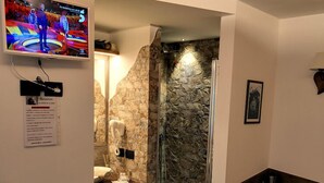 Un baño compacto con pared de piedra, ducha y un rincón de descanso con toalla y artículos de aseo.