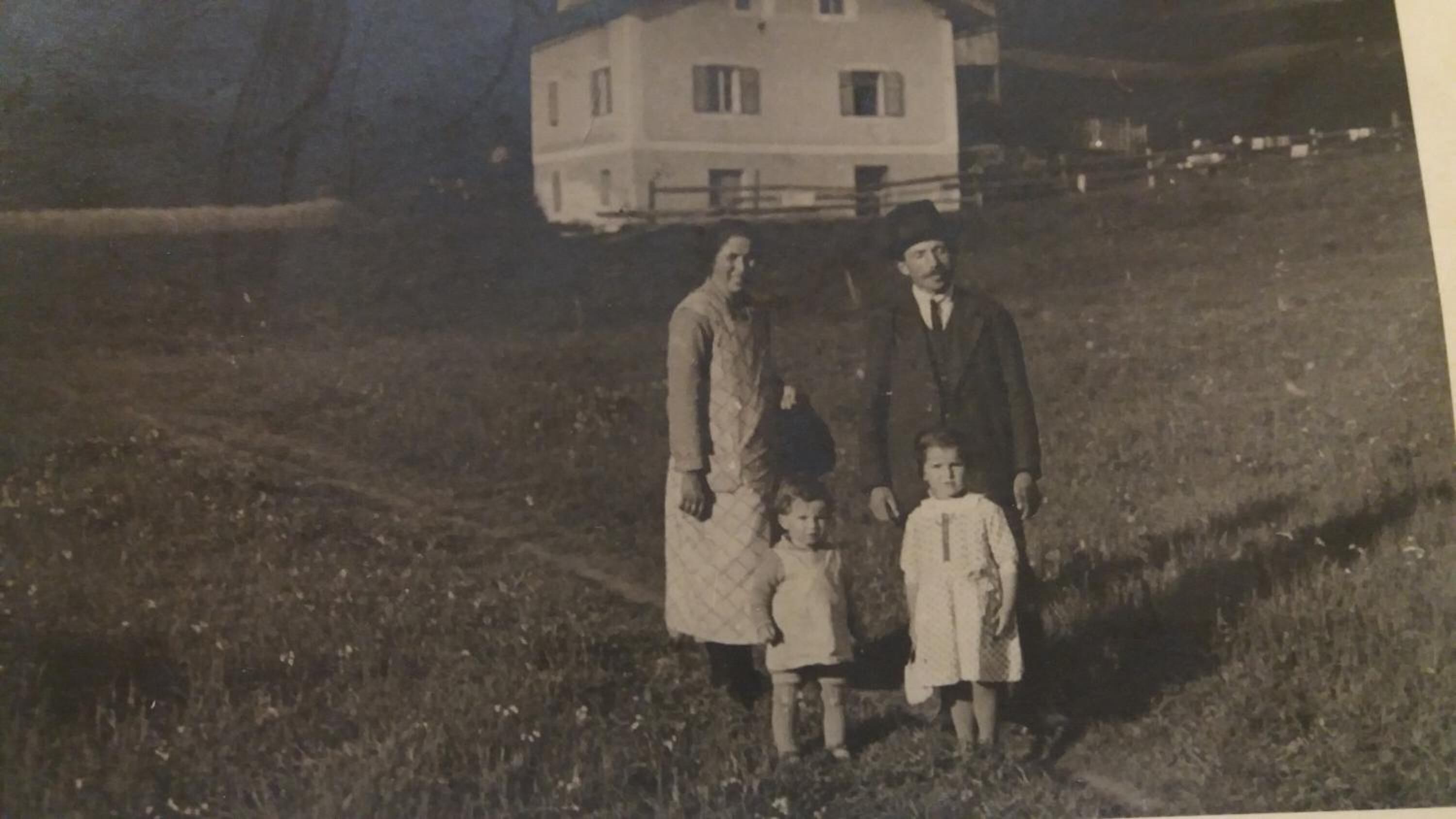 A historical black and white photograph of a family in a grassy field with a large building in the background.