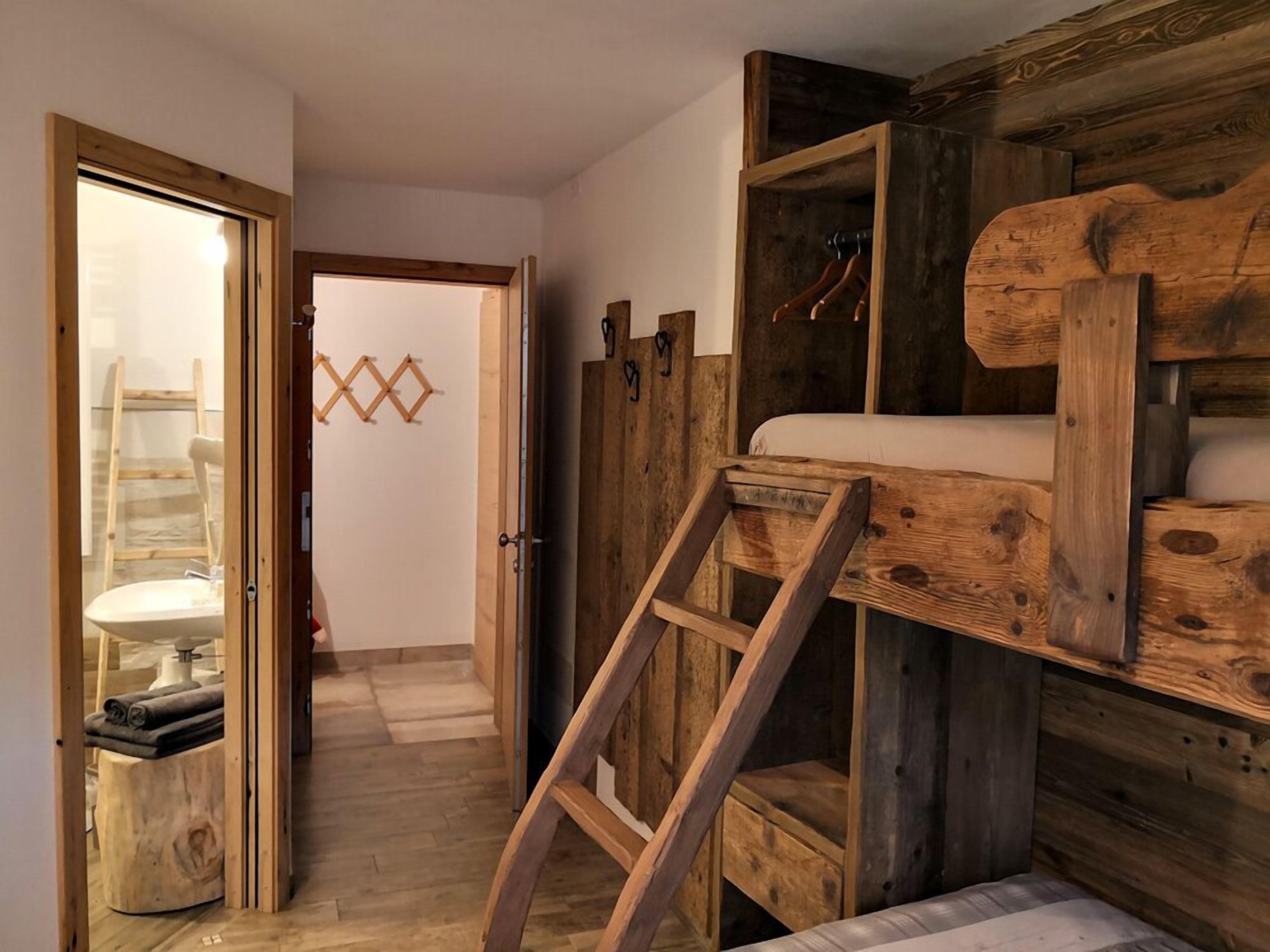 A rustic wooden room with a loft bed, a ladder, and a small bathroom with a sink and towel rack.