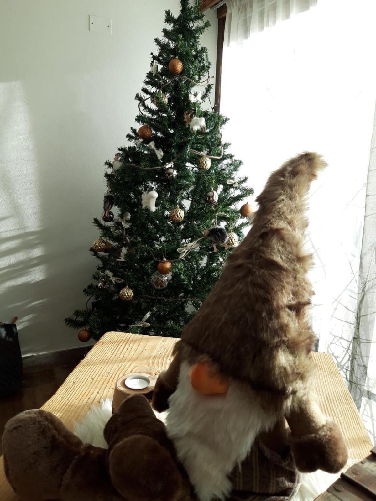 A room with a Christmas tree decorated with ornaments and a plush toy resembling a gnome.