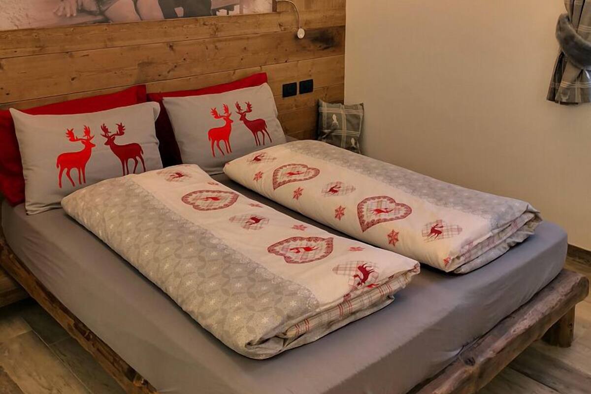 A cozy room with a wooden headboard, a bed with patterned bedding, a wall-mounted lamp, and a rustic wooden floor.