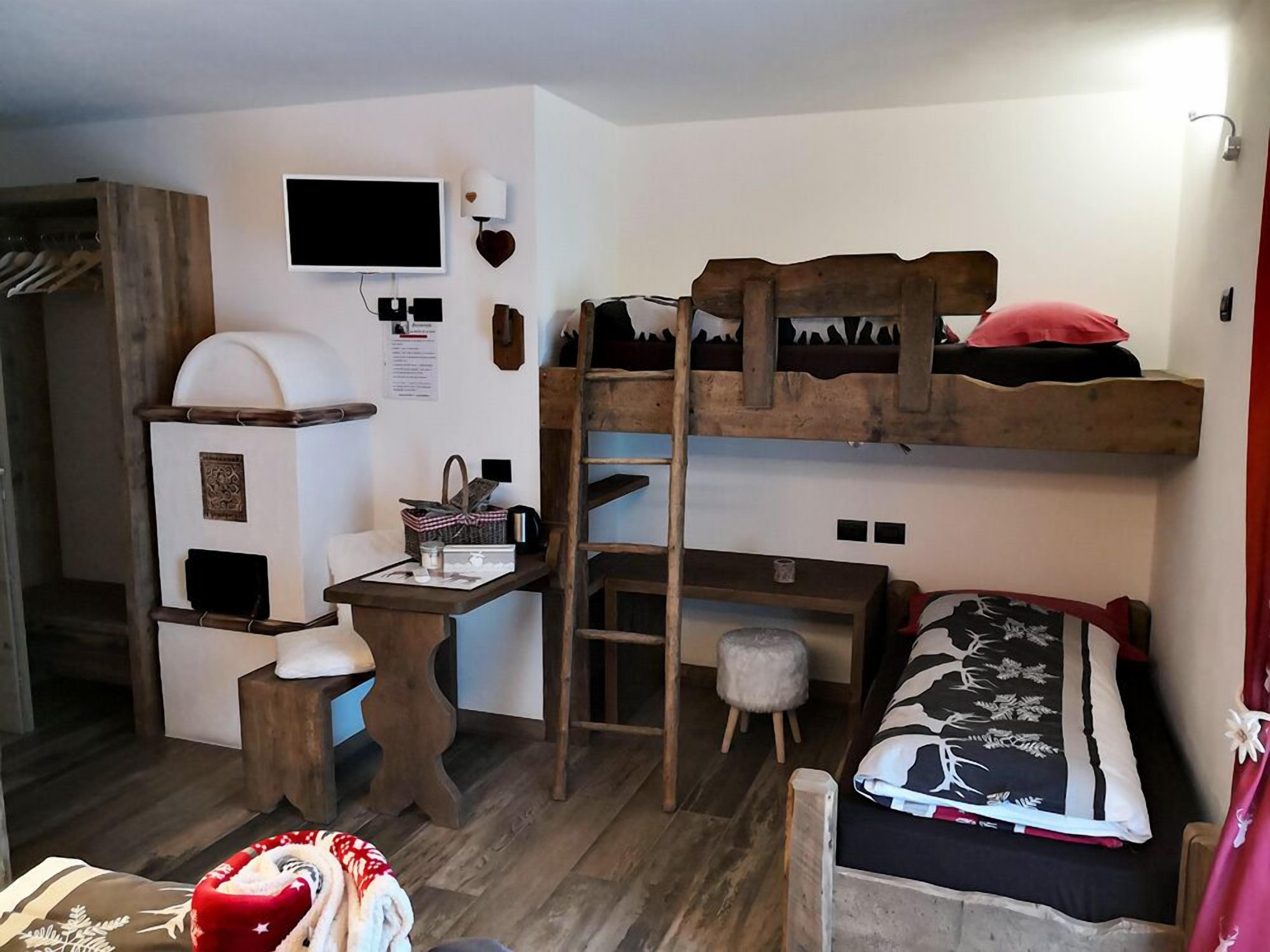 Habitación pequeña con una cama nido, un escritorio, una silla, un taburete, un televisor y un armario.